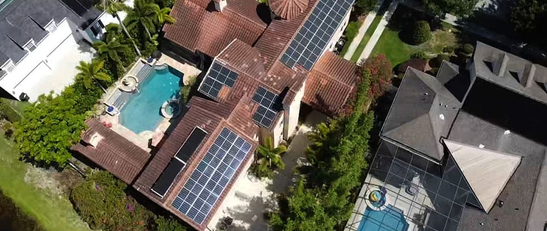 Aerial view of residential solar panel installation on clay tile roof home with swimming pool demonstrating solar roofing integration by Castaways Roofing