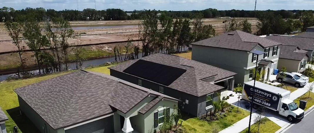 Aerial view of residential solar panel installation on asphalt shingle roof in suburban neighborhood with Castaways Roofing service truck onsite showcasing solar roofing integration by Castaways Roofing