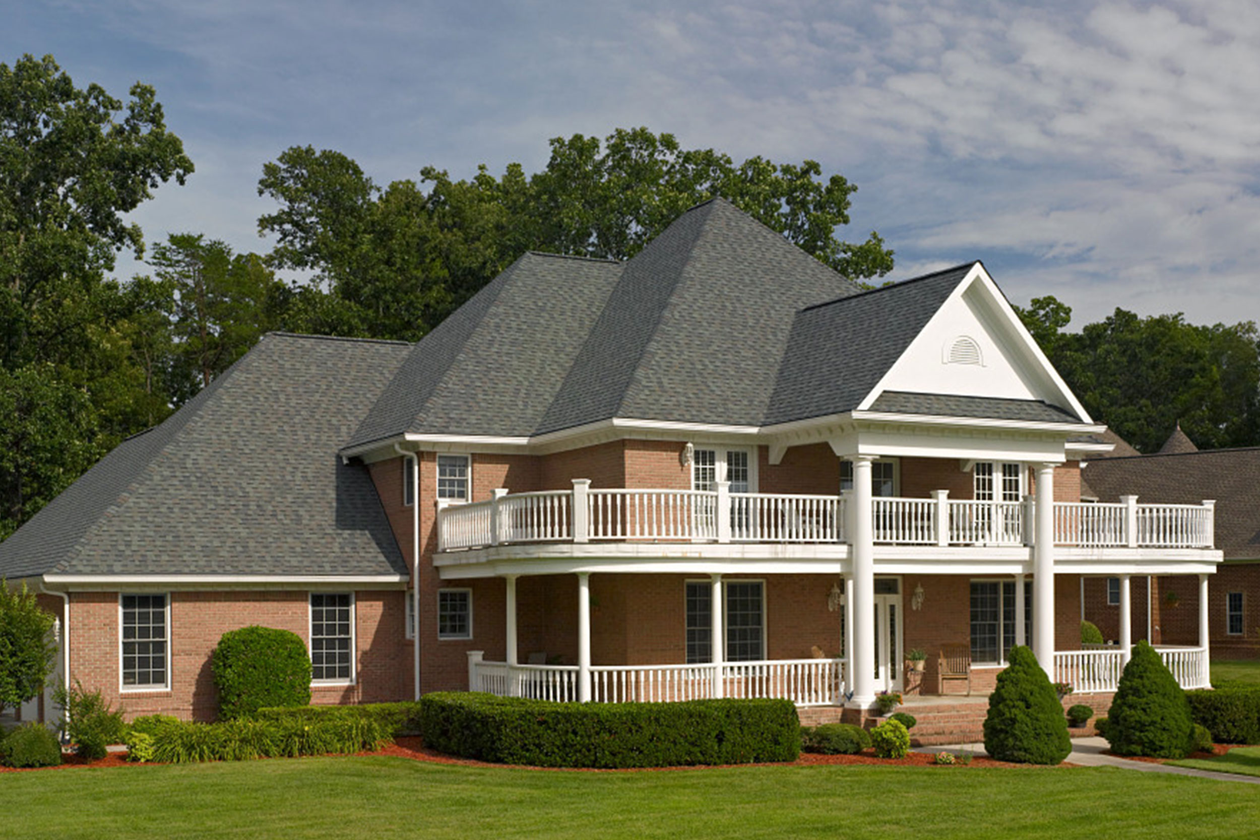 Large brick home with architectural asphalt shingle roof and classic gabled design, showcasing durable residential roofing installation by Castaways Roofing