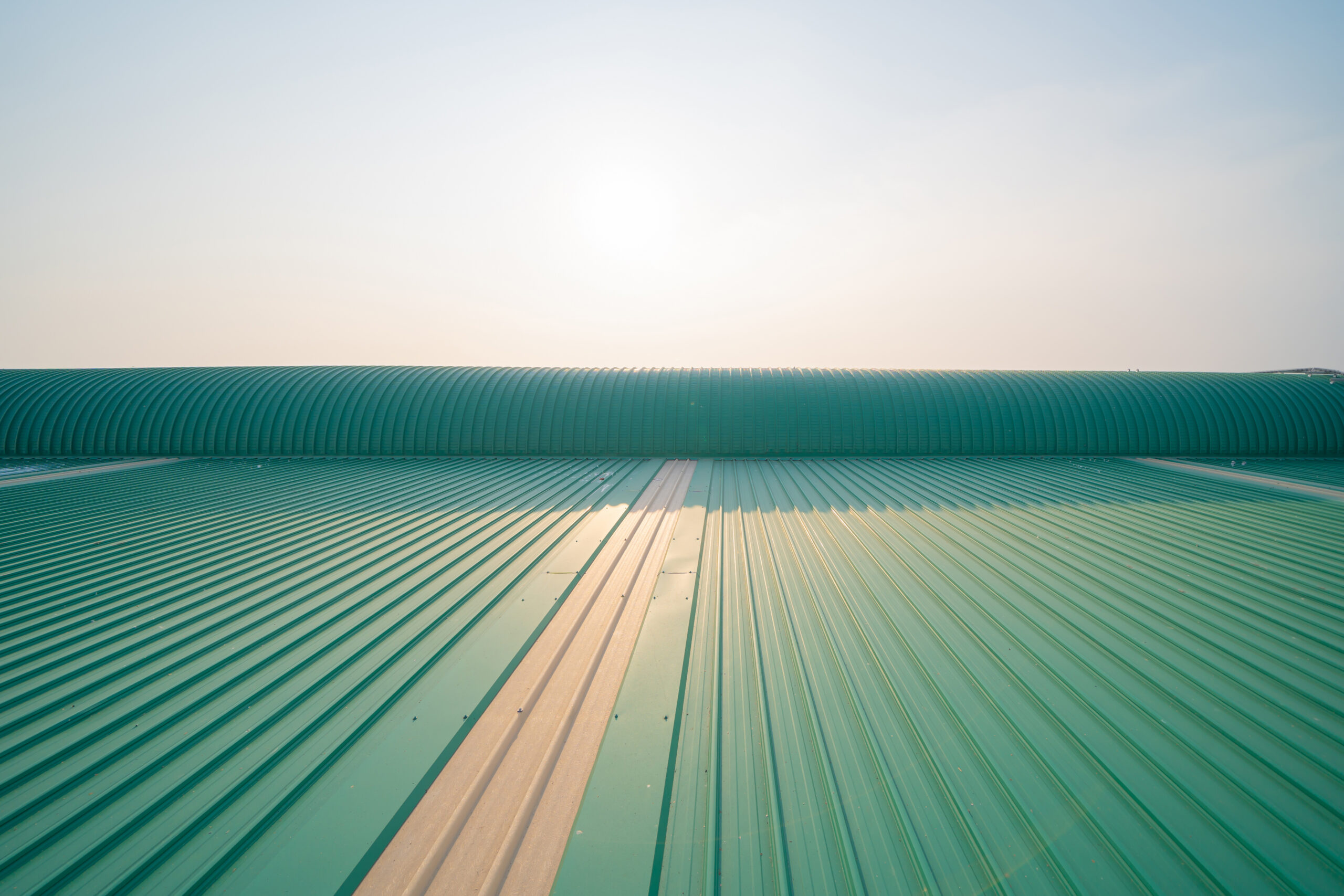 Green standing seam metal commercial roof system with curved architectural ridge detail under clear sky, durable energy-efficient roofing installation for large commercial buildings by Castaways Roofing