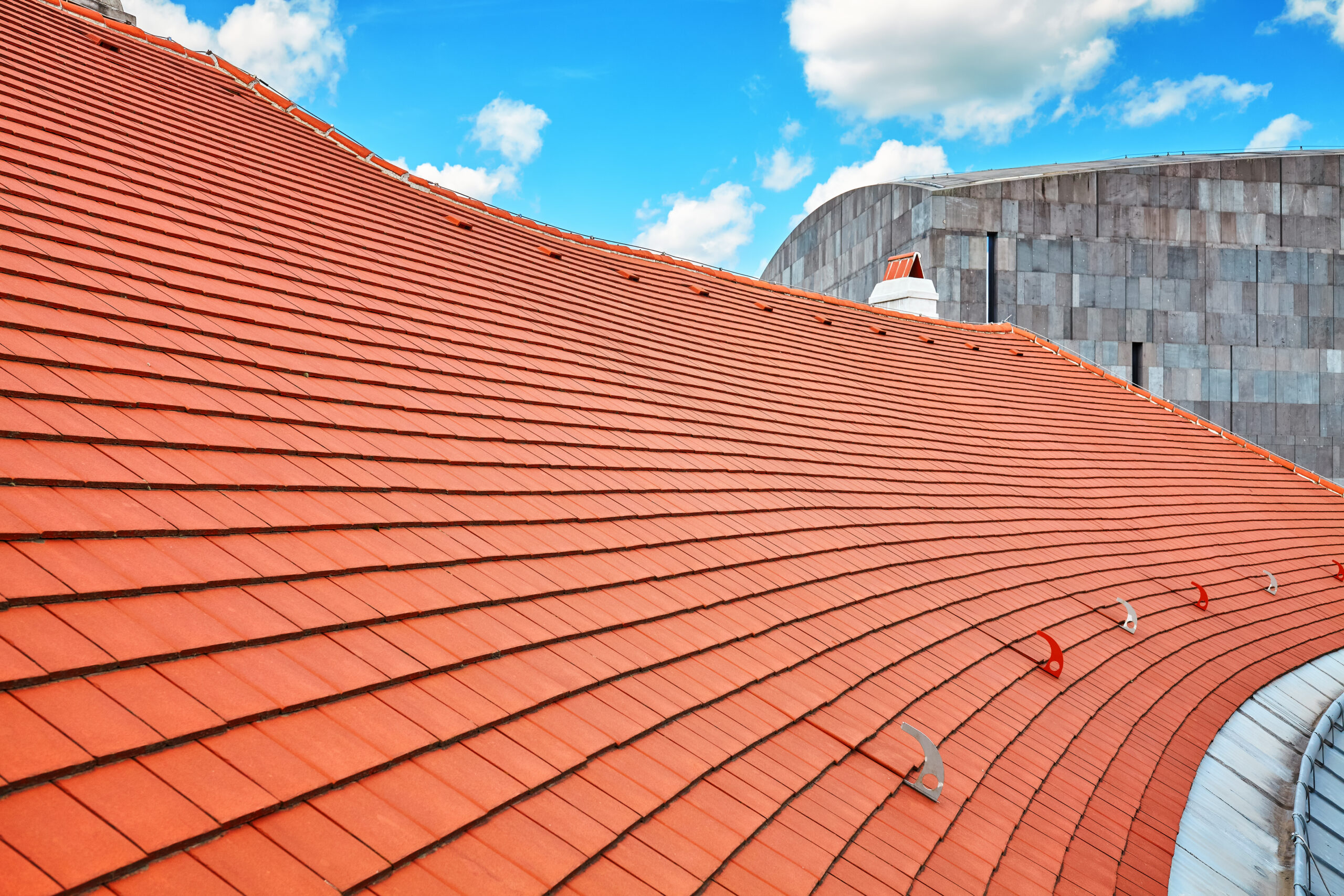 Clay tile commercial roof installation with curved architectural design and roof safety anchors for maintenance access under blue sky, Castaways Roofing commercial roofing system